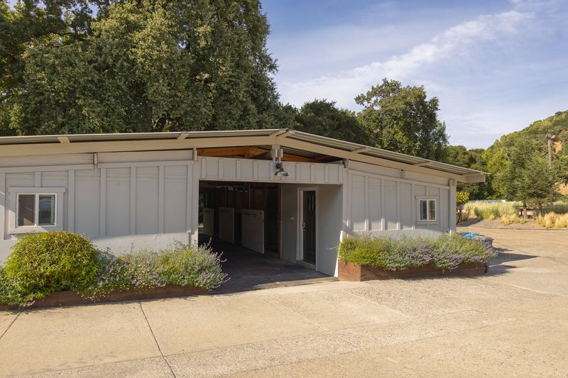 Cream barn exterior with a center breezeway, lavender planters, and oak trees.