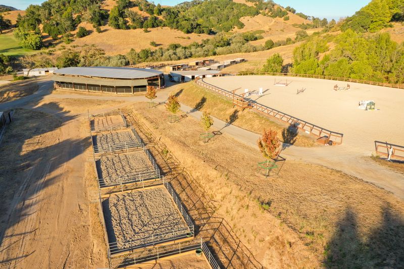 Aerial view across the turnout pens, covered arena, and outdoor jump arena