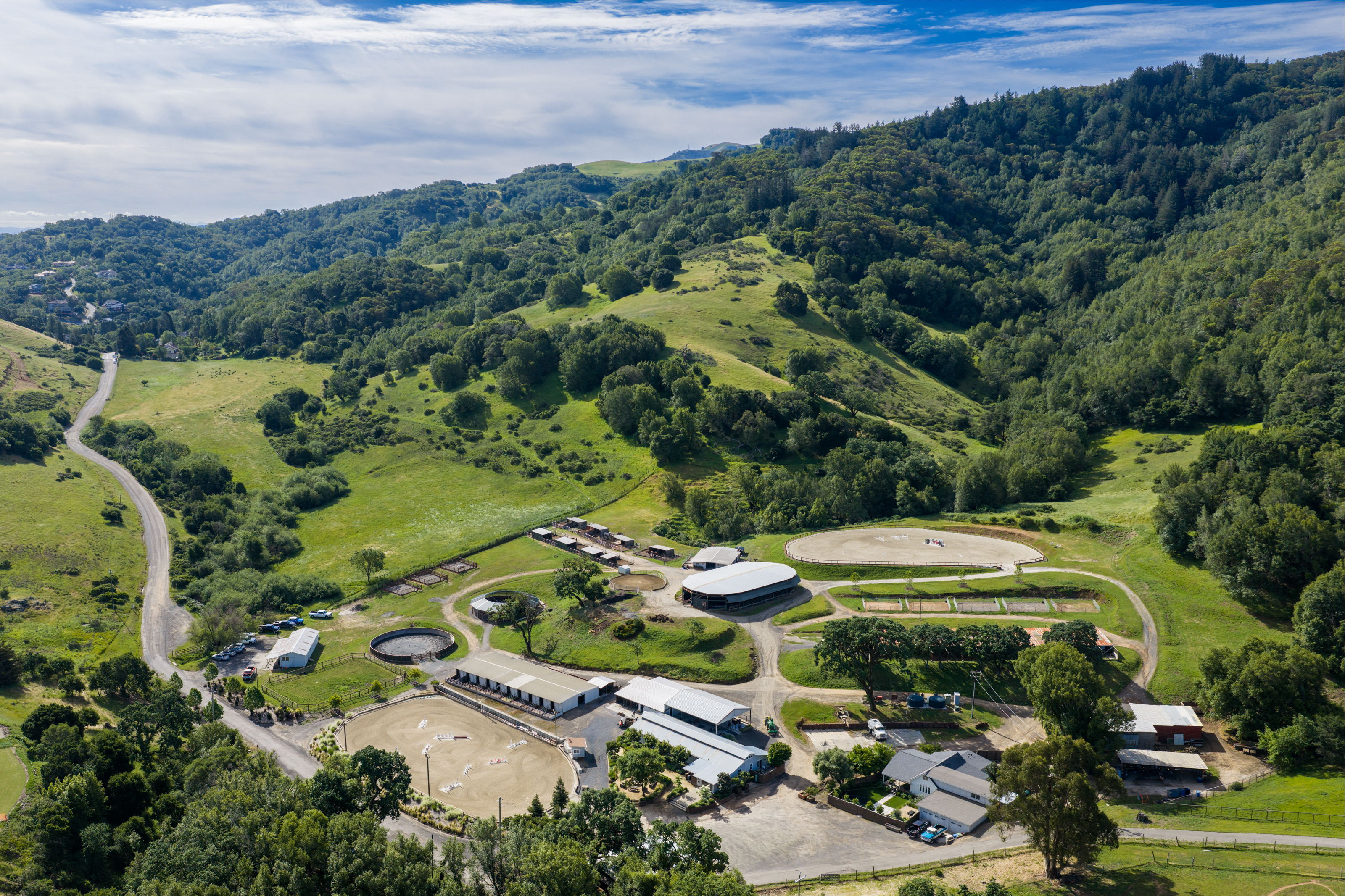 The barns, riding arenas, and round pens at Hindsight Farms beneath green, wooded hills.