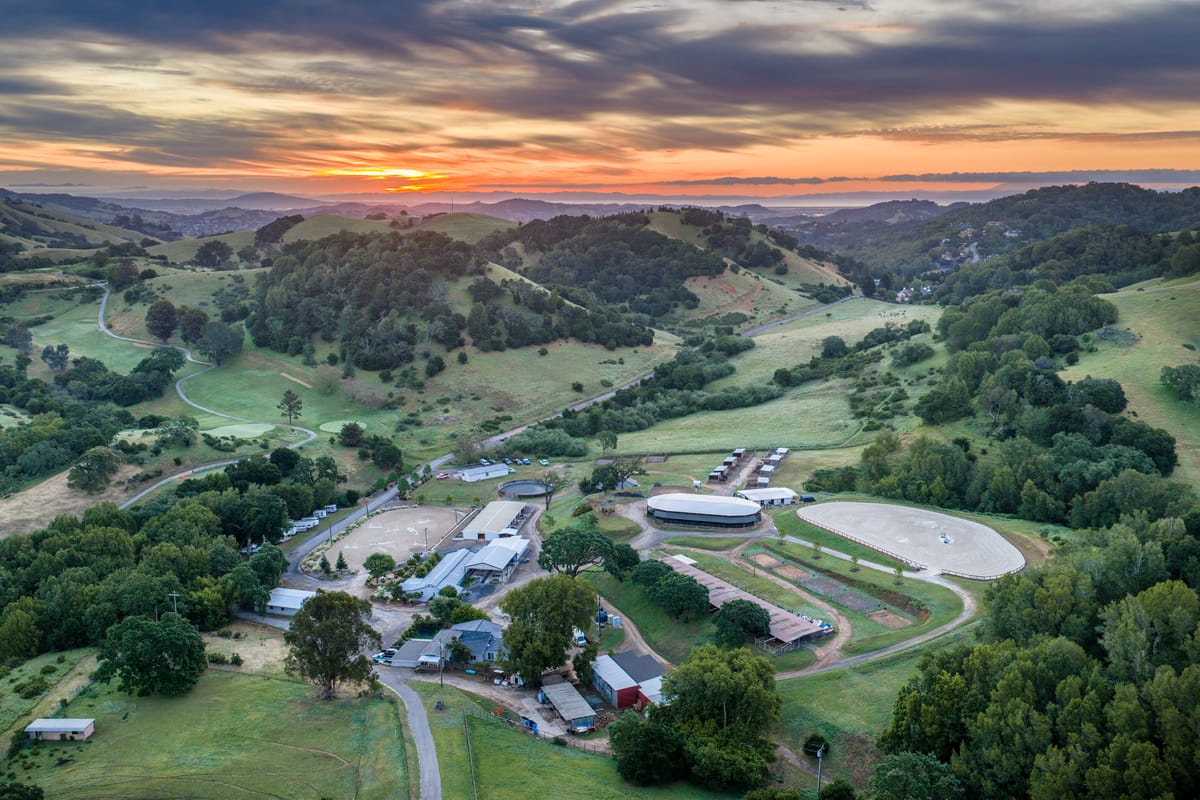 Sunset over Hindsight Farms, with the barns, riding arenas, and round pens among green hills.