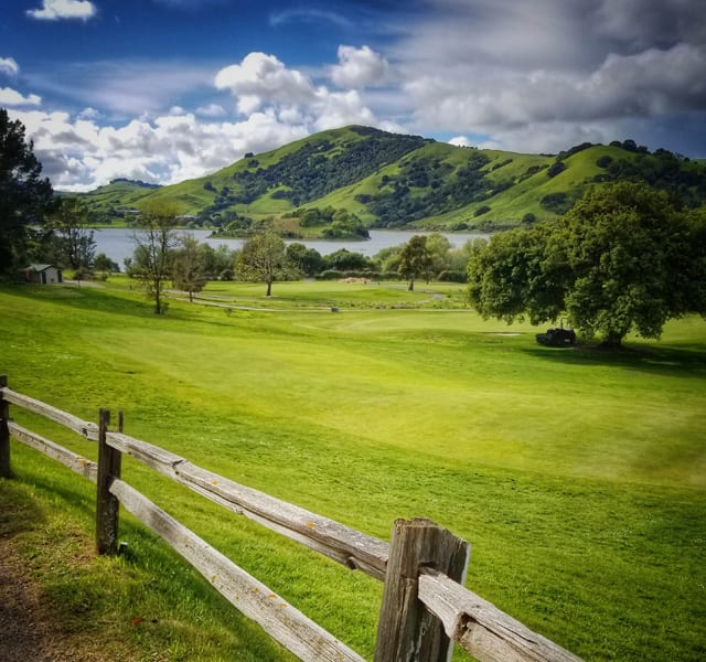 Indian Valley Golf Club fairway beside a wooden fence, with Stafford Lake and green hills beyond.