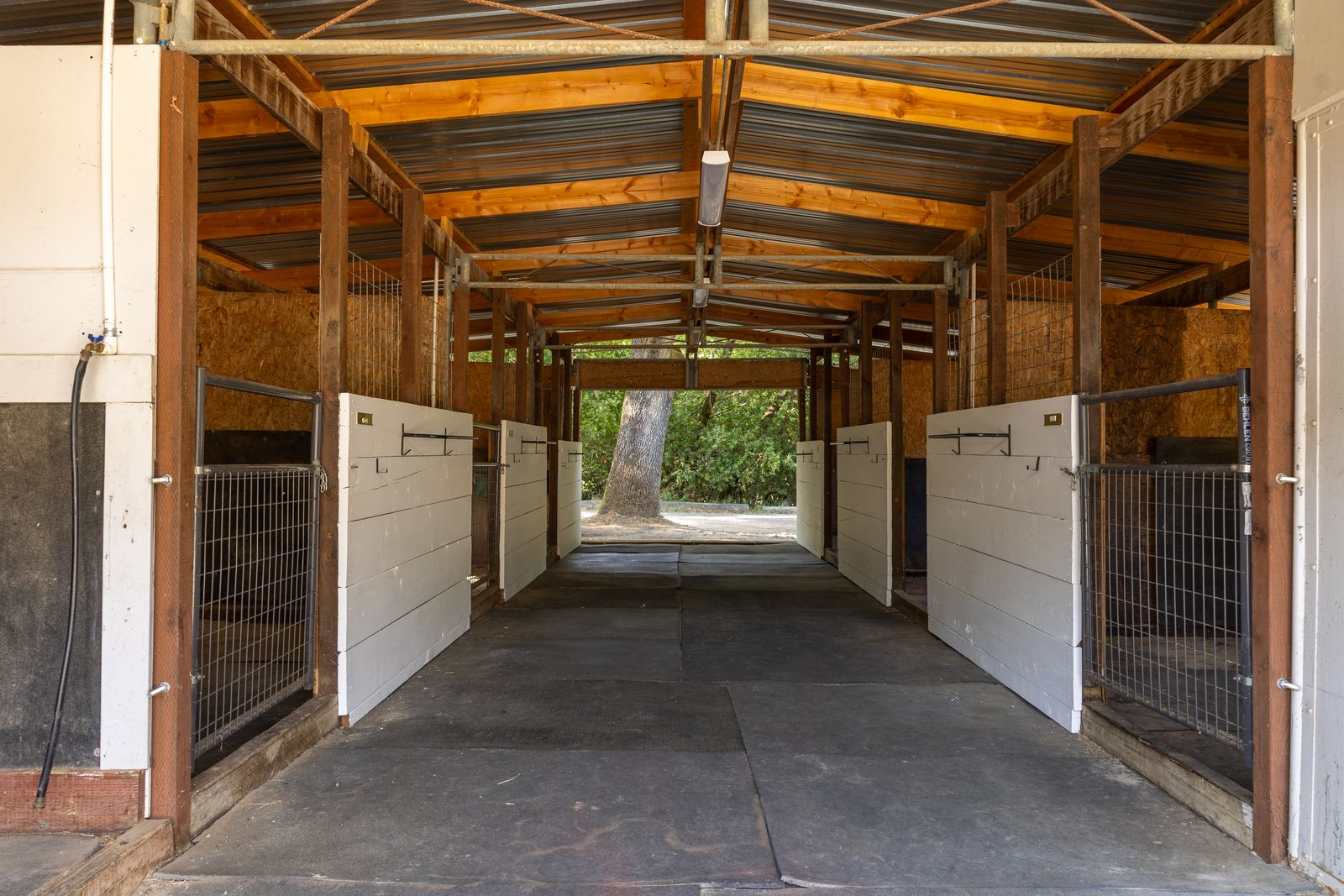 White stall doors and wire-mesh gates along both sides of a covered barn aisle.