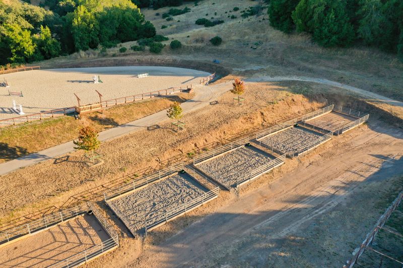 Golden-hour aerial of the turnout pens beside the outdoor jump arena